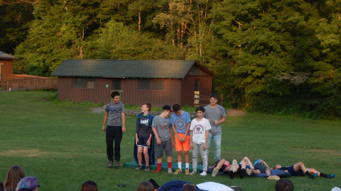 Cabin group standing in a row in front of a mattress. Half the campers have fallen backward onto the mattresses.