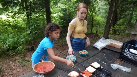Campers adds sauce to bread in a pie iron with counselor supervision.