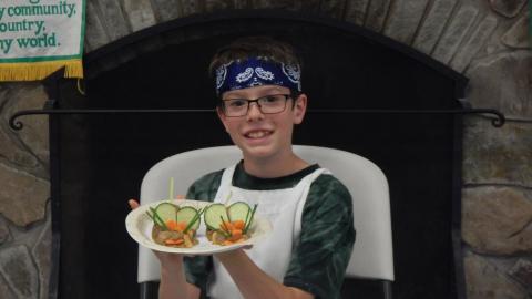 Youth displaying a culinary creation that resembles a mouse made of veggies.