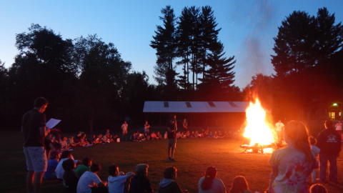 Campers seated in a large circle around a bonfire.