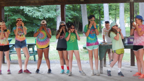 Cabin group wearing tie dye t-shirts and sunglasses flossing their teeth.