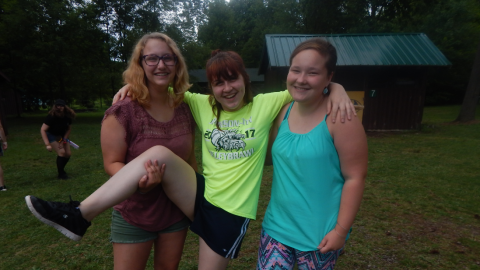 Three campers standing together smiling. One holds up one leg of the middle camper.