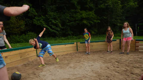 youth in the gaga pit. One youth is leaned far to the side toward a kickball with hands raised behind them and one foot off the ground.
