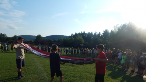 three campers work together to fold the American flag while the rest of camp looks on.