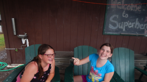two campers sitting in Adirondack chairs and laughing.